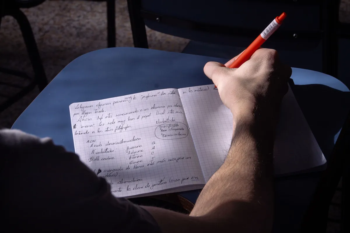 A student writing notes in a sunlit classroom in Buenos Aires.